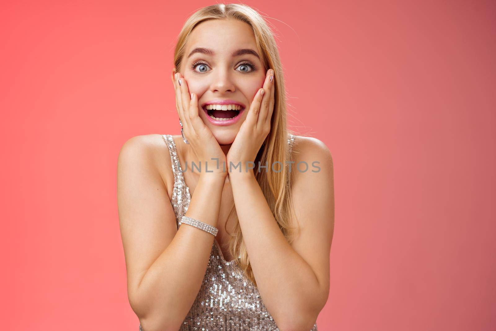 Amazed speechless excited attractive young woman blond long hair press palms cheeks blushing amused cannot believe see popular super star glancing thrilled amazement, surprised red background by Benzoix