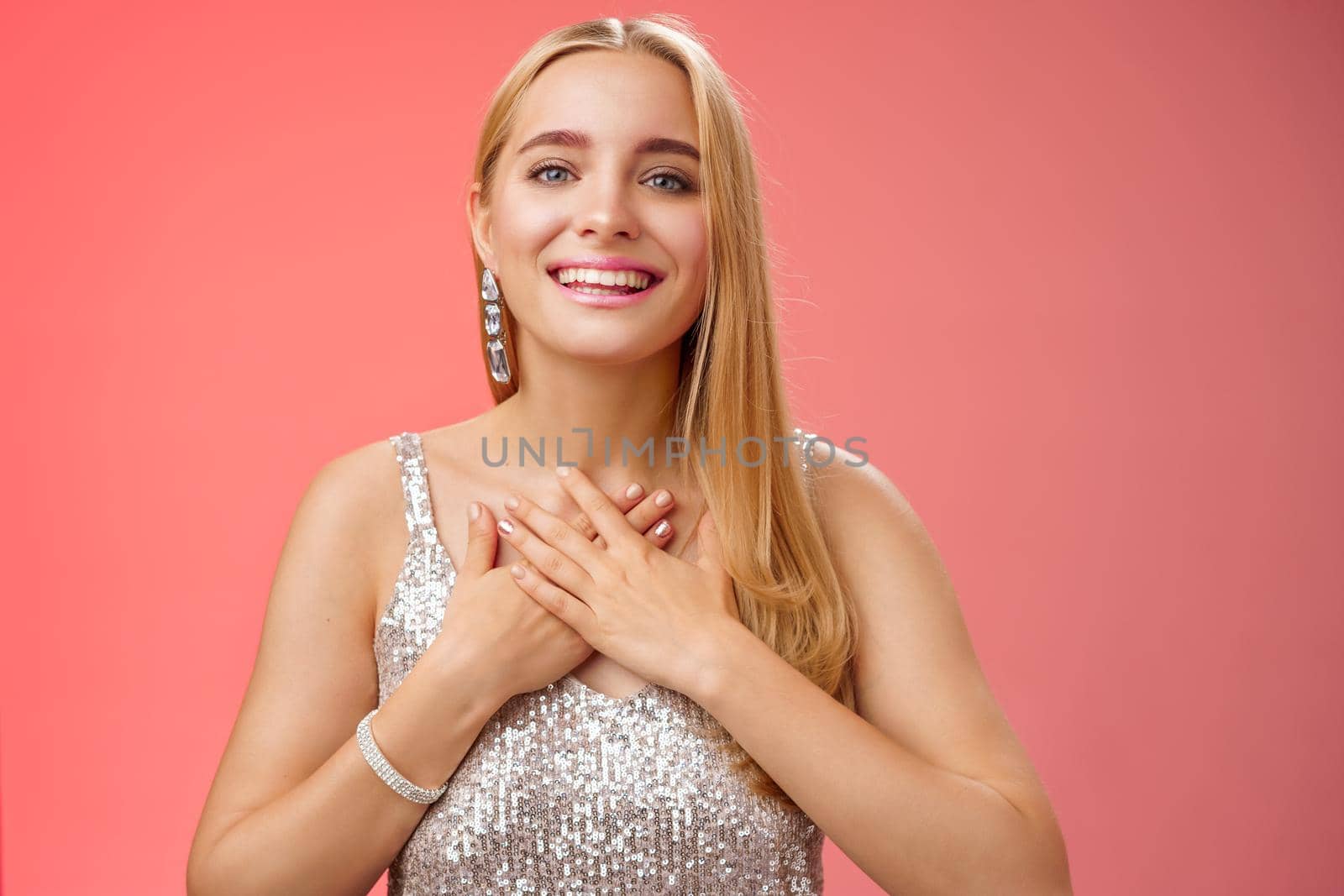 Grateful charming blond european 25s woman in silver party dress press palms heart feel thankful appreciate effort cherish romantic gesture receive flattering compliments gifts, smiling happily.