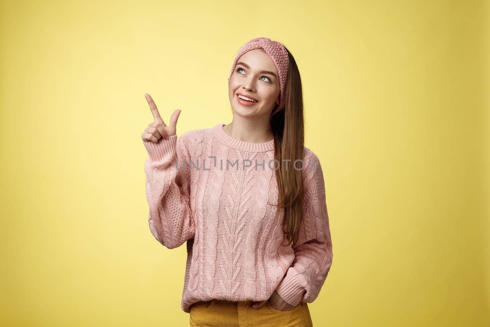 Portrait of amused interested cute 20s european girl wearing sweater, headband looking upper left corner pointing sideways smiling intrigued, ecstatic, captured by curious promo over yellow wall by Benzoix