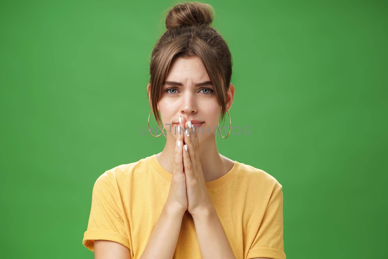 Waist-up shot of nervous upset girlfriend holding hands in pray over lips frowning looking concerned worrying for boyfriend standing anxious and sad over green background. Emotions and body language concept