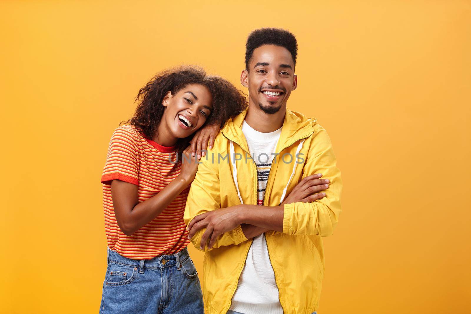 Awesome when boyfriend is best friend. Portrait of charming friendly african american woman leaning on guy touching his shoulder feeling happy they together and she can rely on posing orange wall by Benzoix