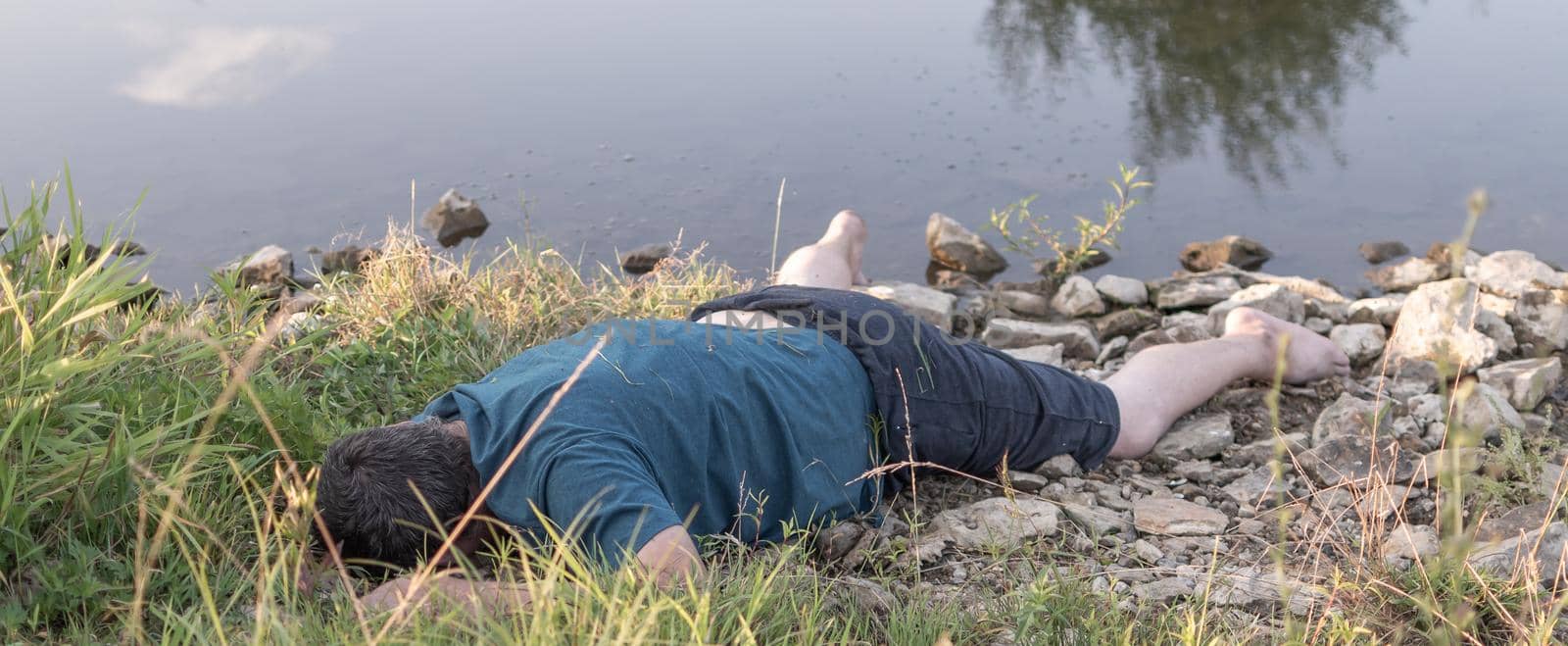 a lifeless dead body lies on the shore of a lake, a young man killed by water. artistic photo painting, selective focus ,
