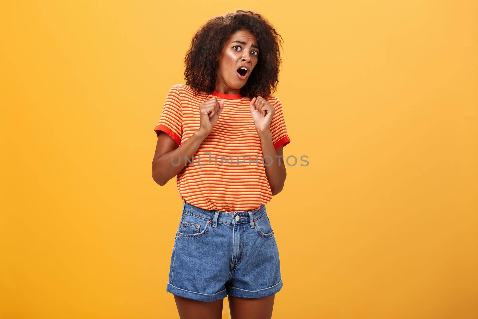 No do not hurt me. Scared silly and insecure good-looking african american woman in stupor screaming for help turning away raising palms near body in defence standing in fright over orange wall. Copy space