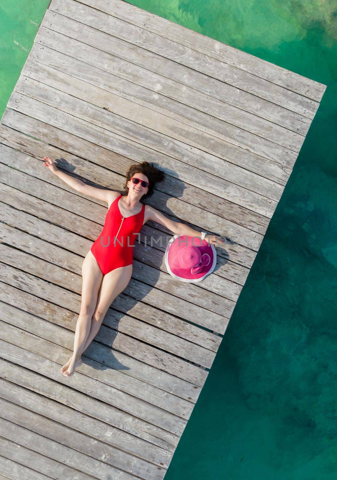 Top view of woman lying down on wooden pier at sunny summer day in Cancun, Mexico. Young sexy woman in the red swimwear on Caribbean. Summer beach vacation concept by Mariakray