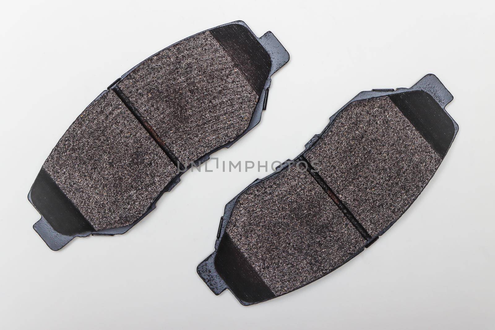 Two brake pads on a flat surface diagonally. Set of spare parts for car brake repair. Details on white background, copy space available. UHD 4K.