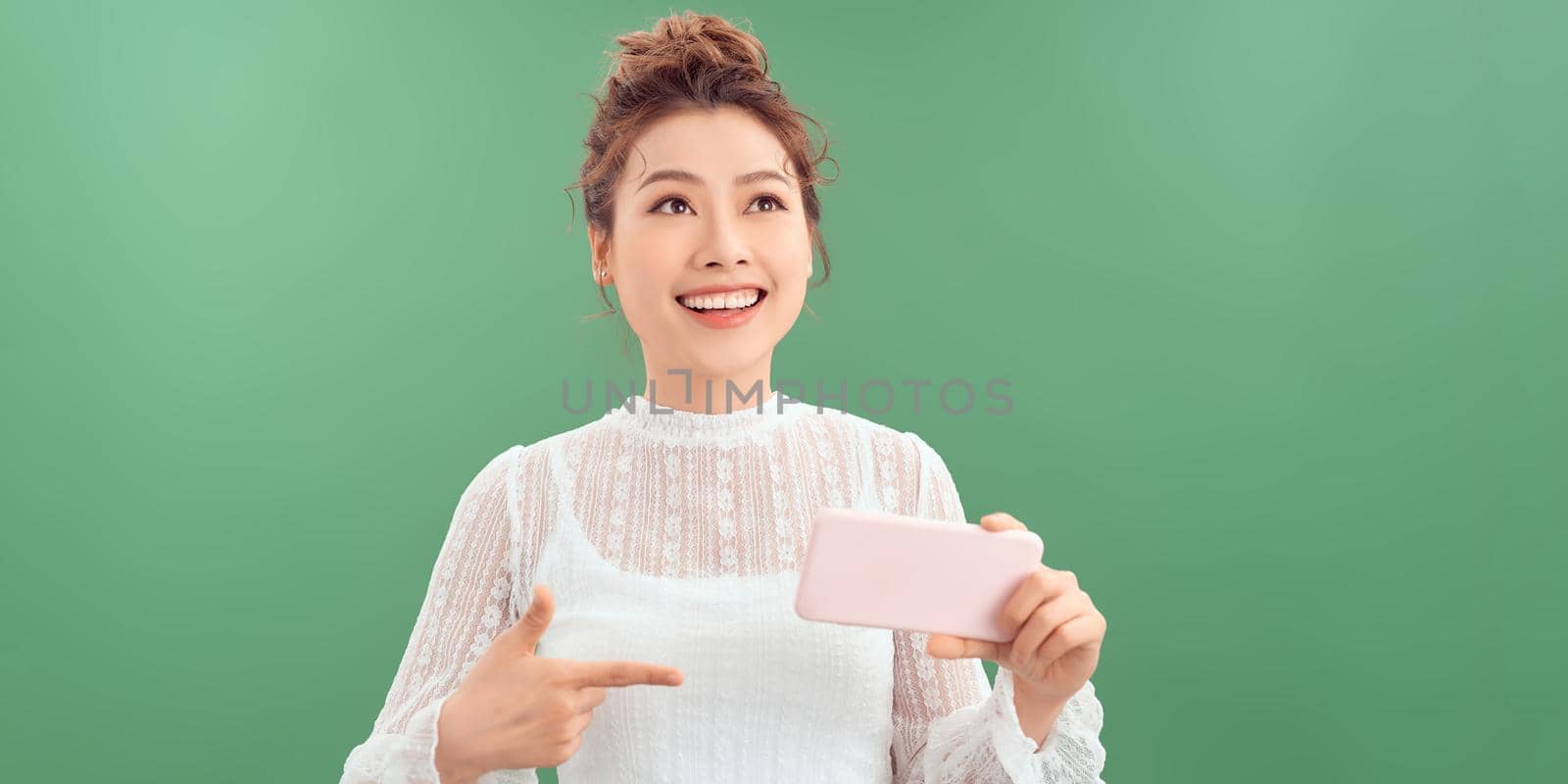Portrait of a smiling casual woman holding smartphone over green background.