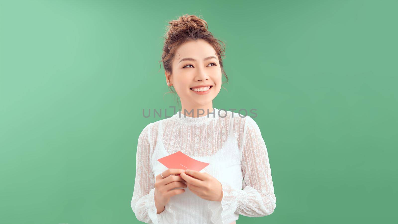 surprised asian young woman holding greeting card while standing isolated on green by makidotvn