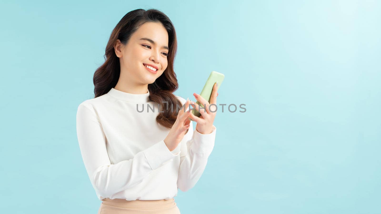 Modern lifestyle and communication. Smiling beautiful girl talking on phone while standing on blue background  by makidotvn