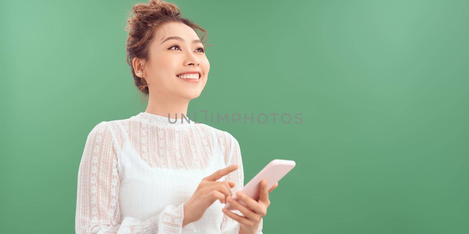 Photo of cheerful cute beautiful young woman chatting by mobile phone isolated over green wall background. Looking aside. by makidotvn