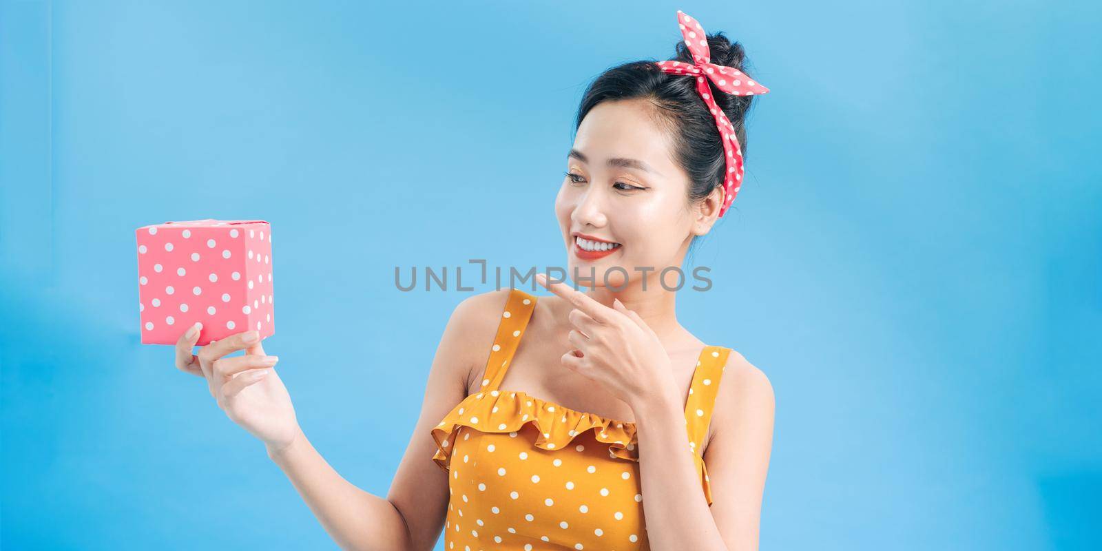 Cheerful young woman holding small gift box isolated on a blue background and looking at camera