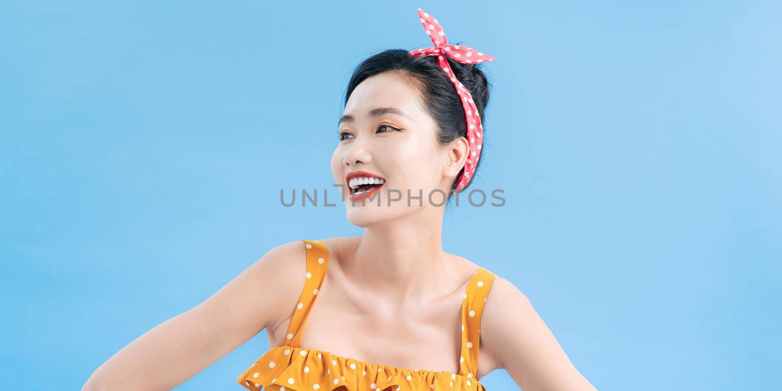 Young beautiful woman posing in new casual yellow and white dotted dress on a blue background