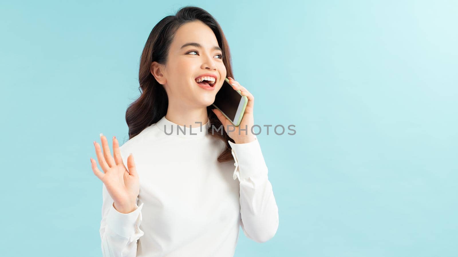 Modern lifestyle and communication. Smiling beautiful girl talking on phone while standing on blue background 