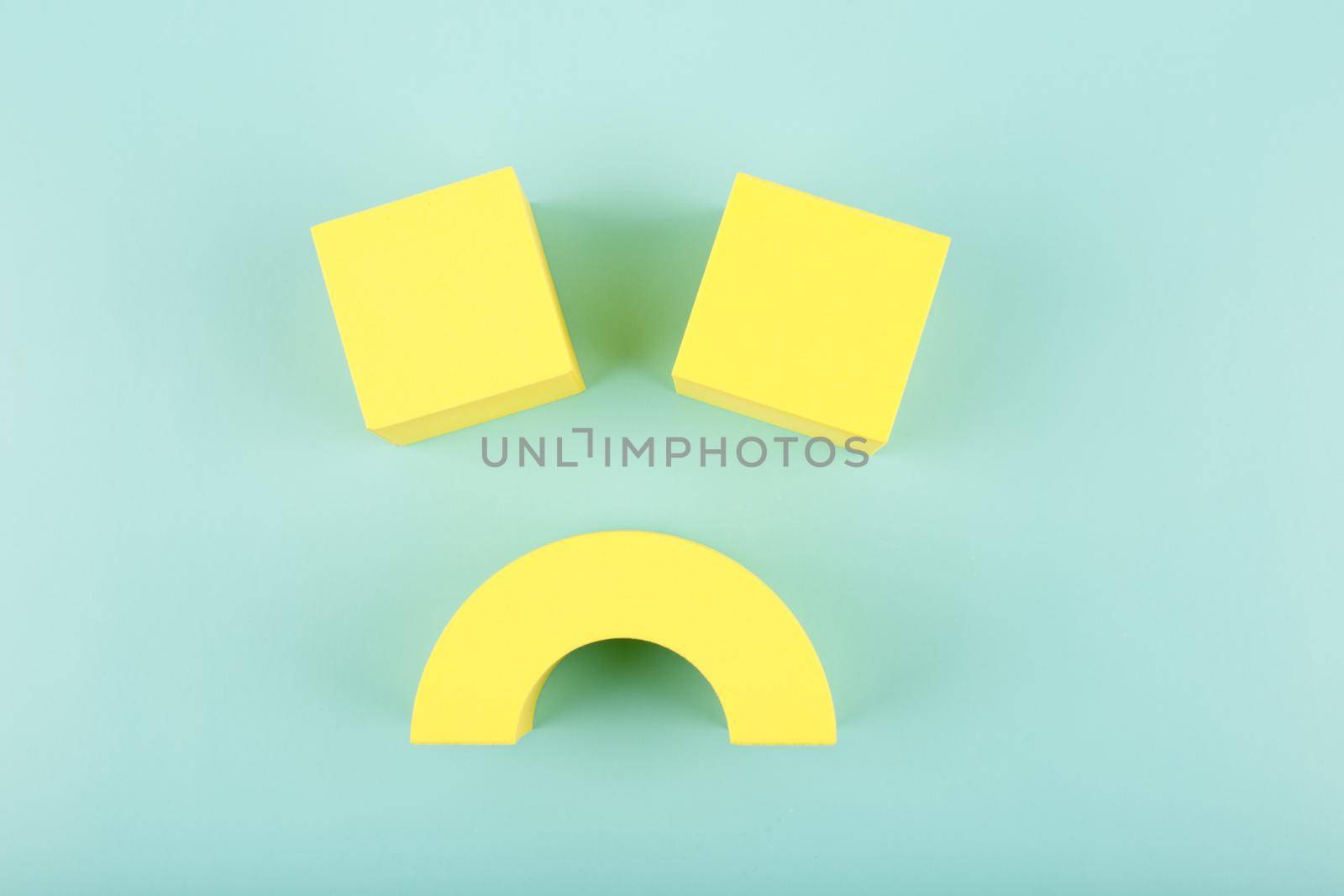 Creative flat lay with unhappy, sad smile symbol made of yellow figures on blue background. Concept of emotions, emoji, mental health or unsatisfied customer or bad service