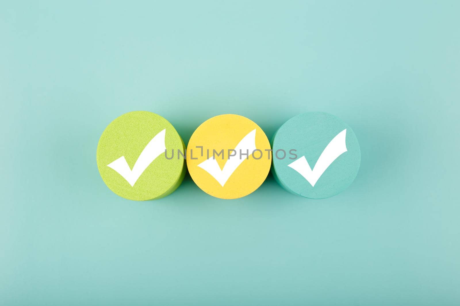Three white checkmarks on multicolored toy circles in a row in the middle on bright aqua blue background. Concept of questionary, checklist, to do list, planning, business or verification.