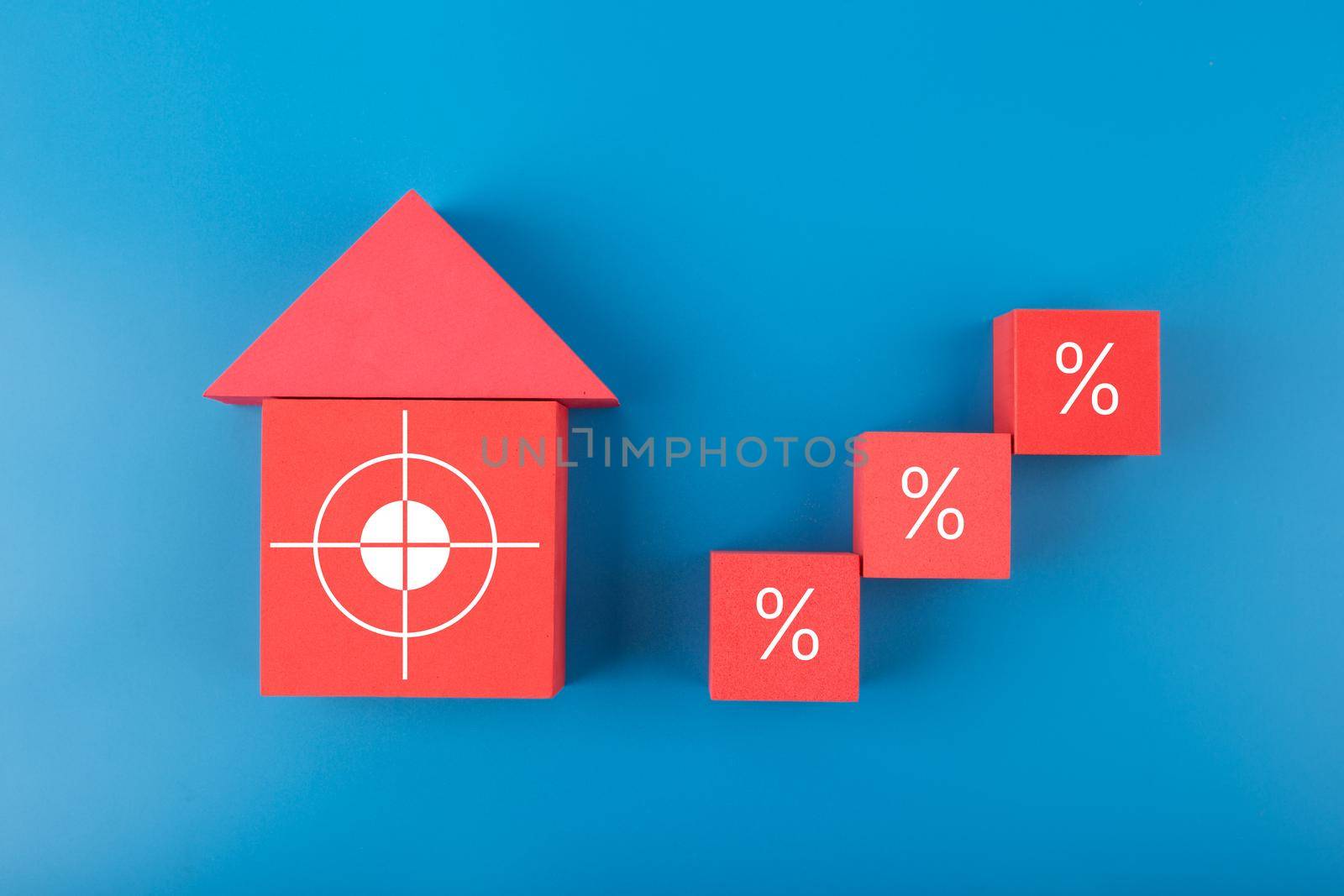 Red house made of toy blocks and ladder made of cubes with increasing percentage sign on blue background. Modern concept of inflation, percent, mortgage, interest rate growth and increasing