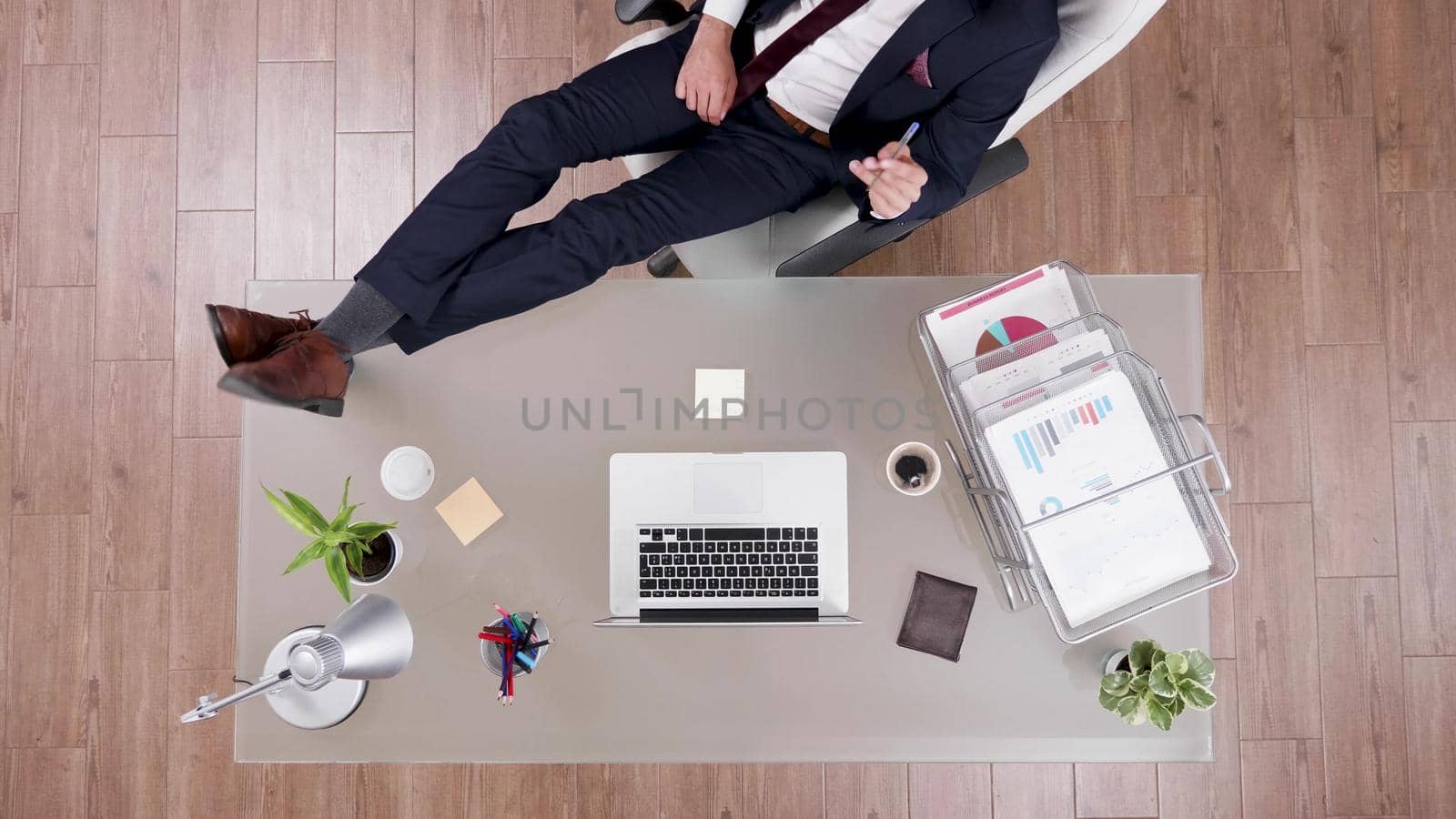 Top view of businessman in suit staying relaxed with feet on office desk by DCStudio