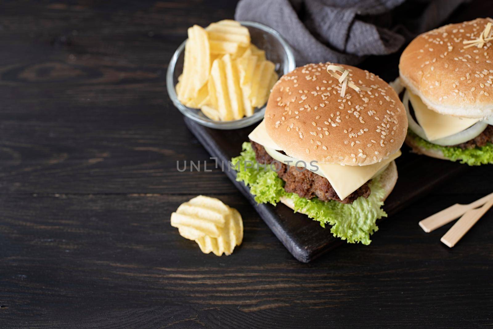 A set of homemade delicious burgers of beef, onion, cheese and lettuce on a dark wooden background. Fat unhealthy food close-up. With copy space.