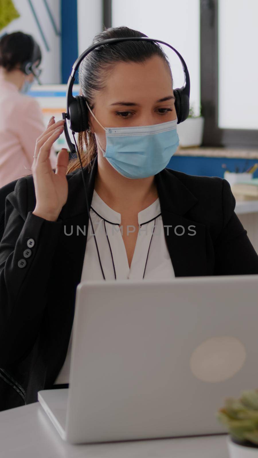 Close up of businesswoman with face mask wearing headset talking into microphone by DCStudio