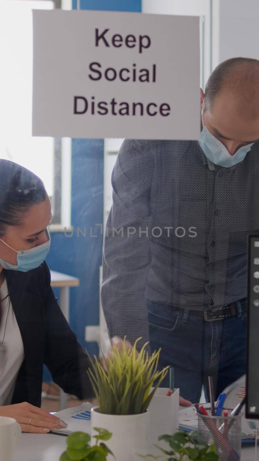 Business people with medical face masks sitting in new normal company office analysing financial project during covid19 pandemic. Coworkers keeping social distancing to avoid virus disease