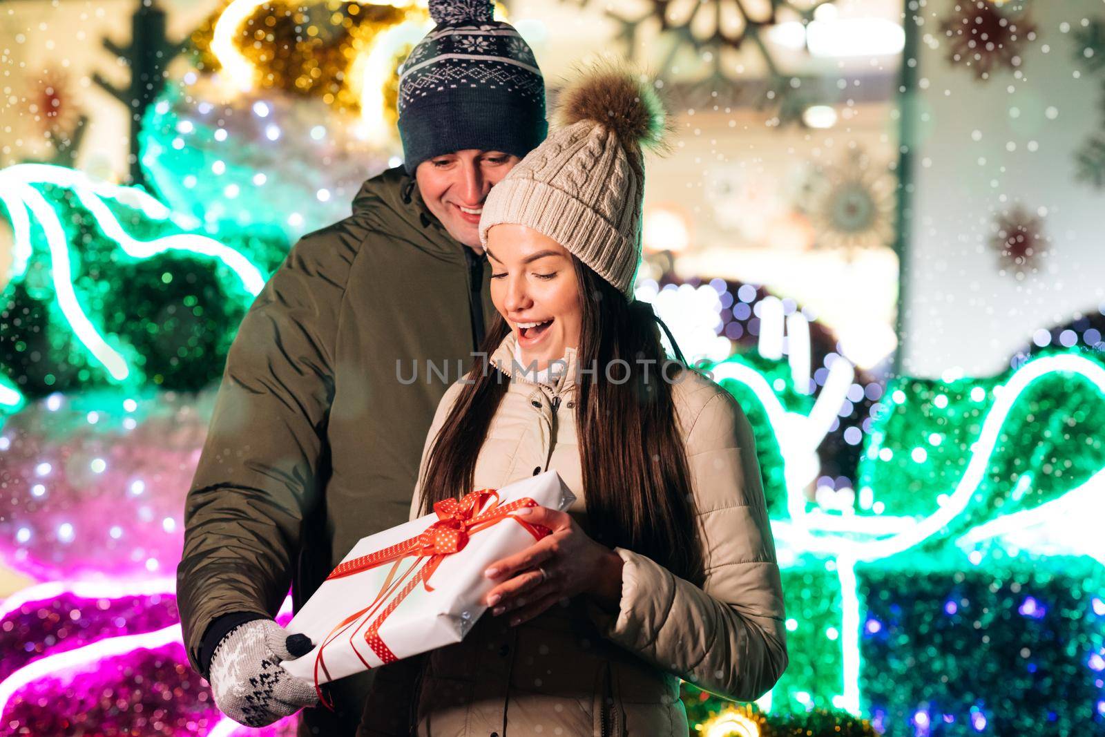 Young happy couple in love taking funny selfies on a smart phone in the Christmas atmosphere. Christmas decorated. Exchange of gifts. Christmas present to beautiful woman by uflypro