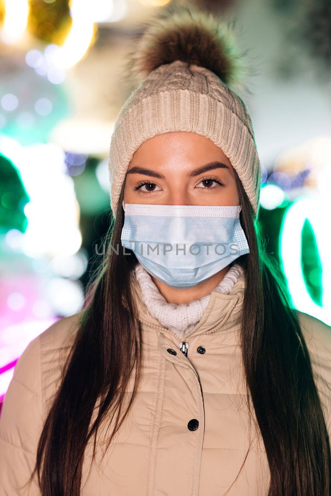 Close up portrait of Caucasian female in medical face mask standing in decorated xmas city. Crowd people sick covid-19. Epidemic coronavirus. Pandemic flu corona virus