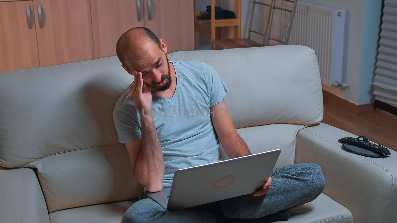 Tired man sitting on sofa while talking with collegue during business videocall conference by DCStudio