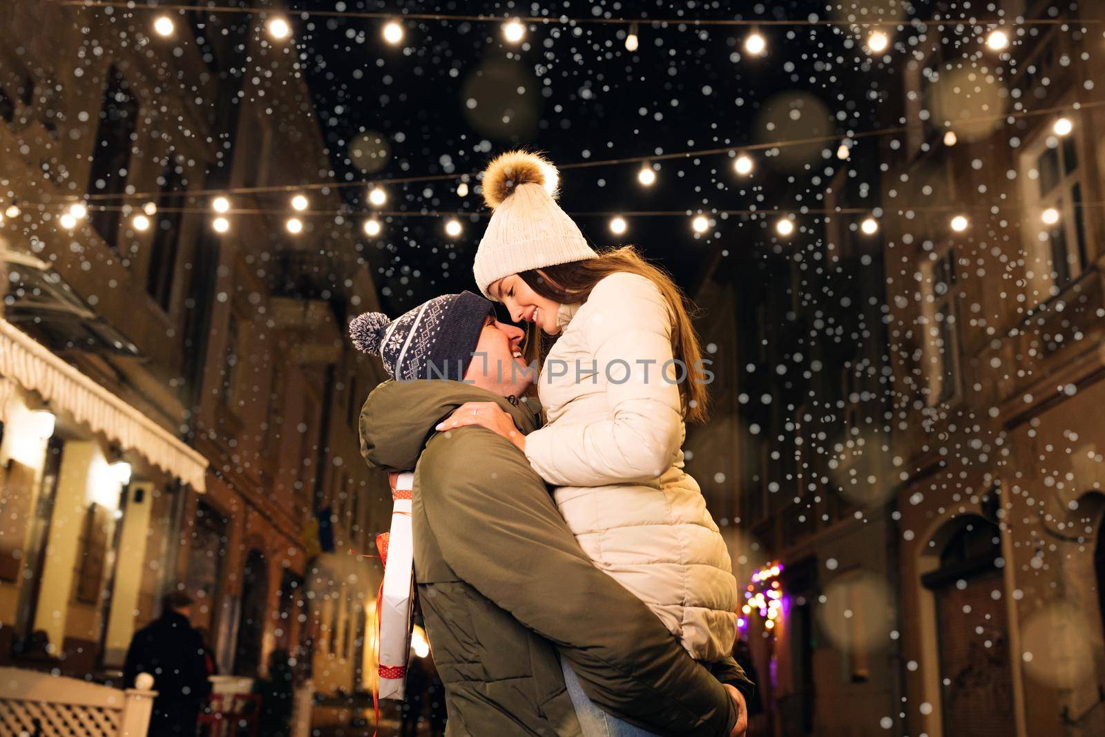 Christmas gifts exchange. Xmas celebration together. Smiling couple celebrating Xmas eve together at bright garland decoration