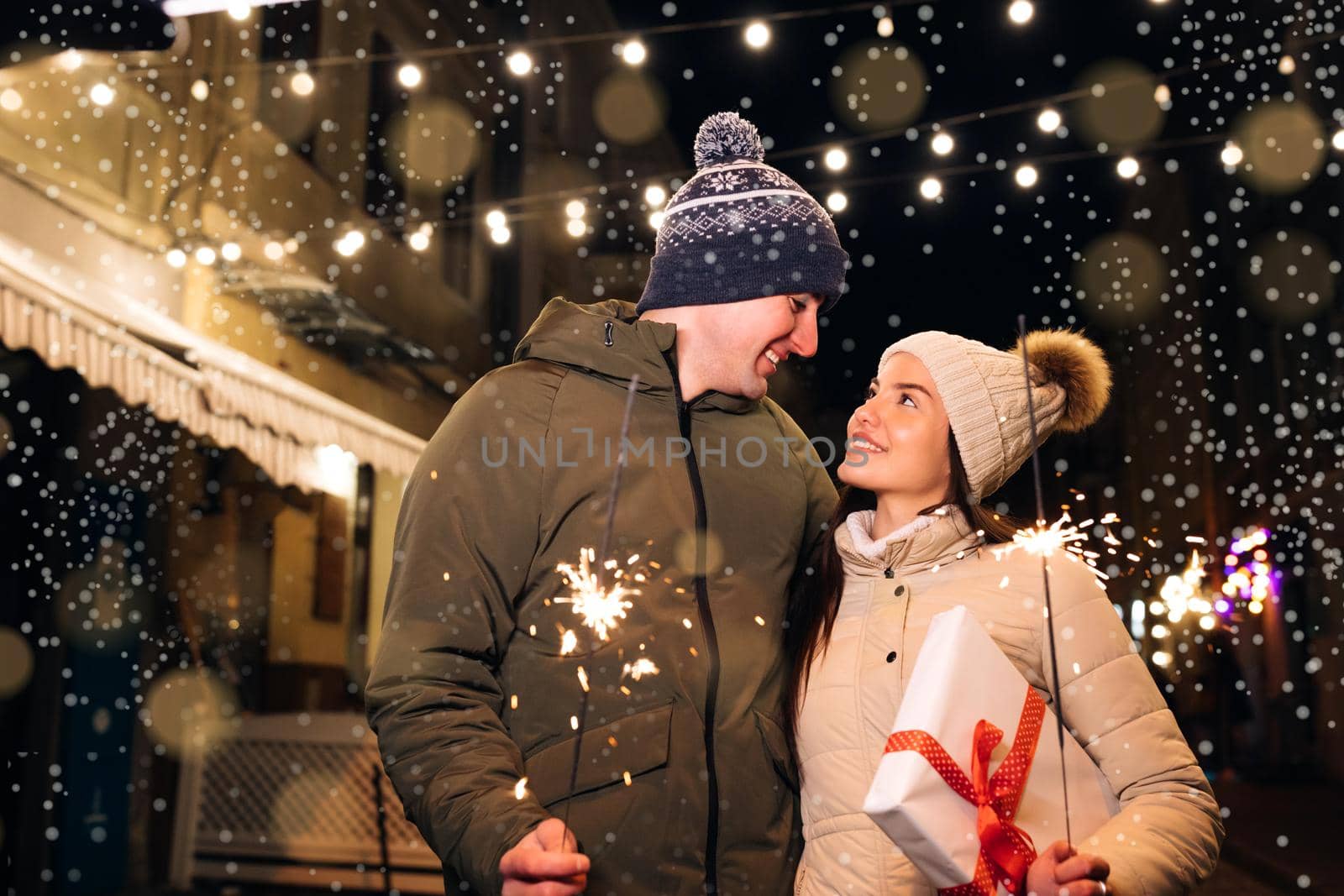 Two people celebrate New Year on the street. Close up portrait of young happy couple standing on the street hugging holding sparklers. Young couple in love holds sparklers in their hands by uflypro