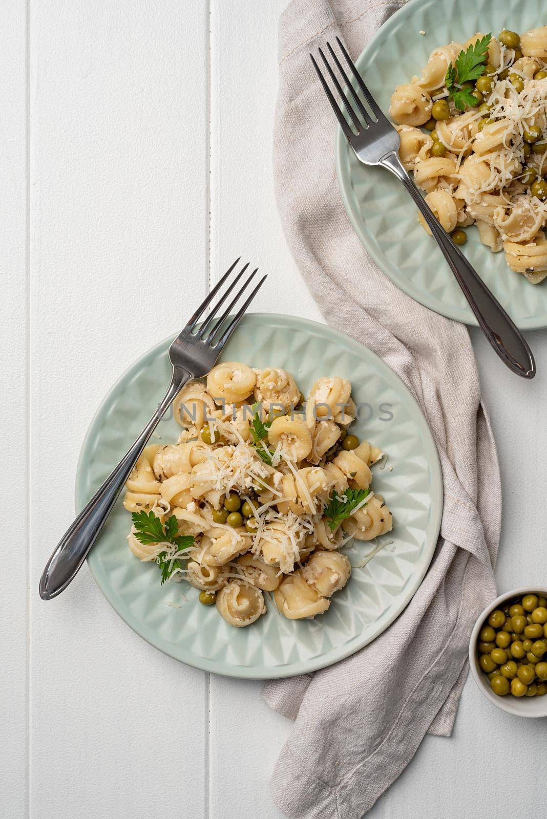 radiatori pasta with cherry tomatoes, cheese and parsley in white plate on wooden background, top view copy space