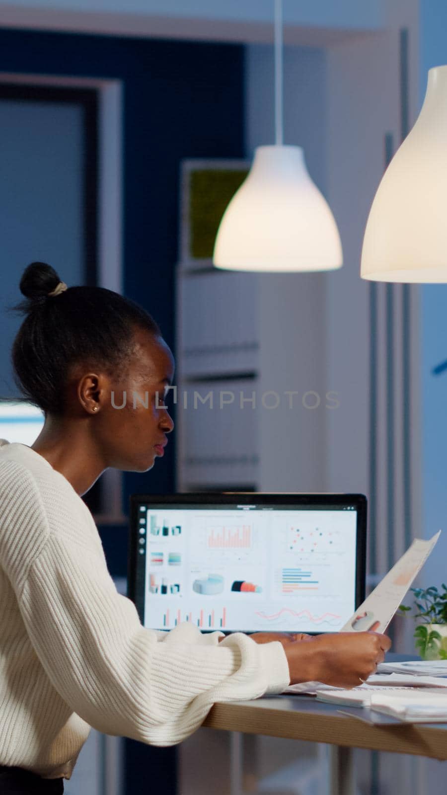 African businesswoman reading business reports from laptop in start up office late night typing new project. Focused employee doing overtime for job respecting deadline of project writing, searching