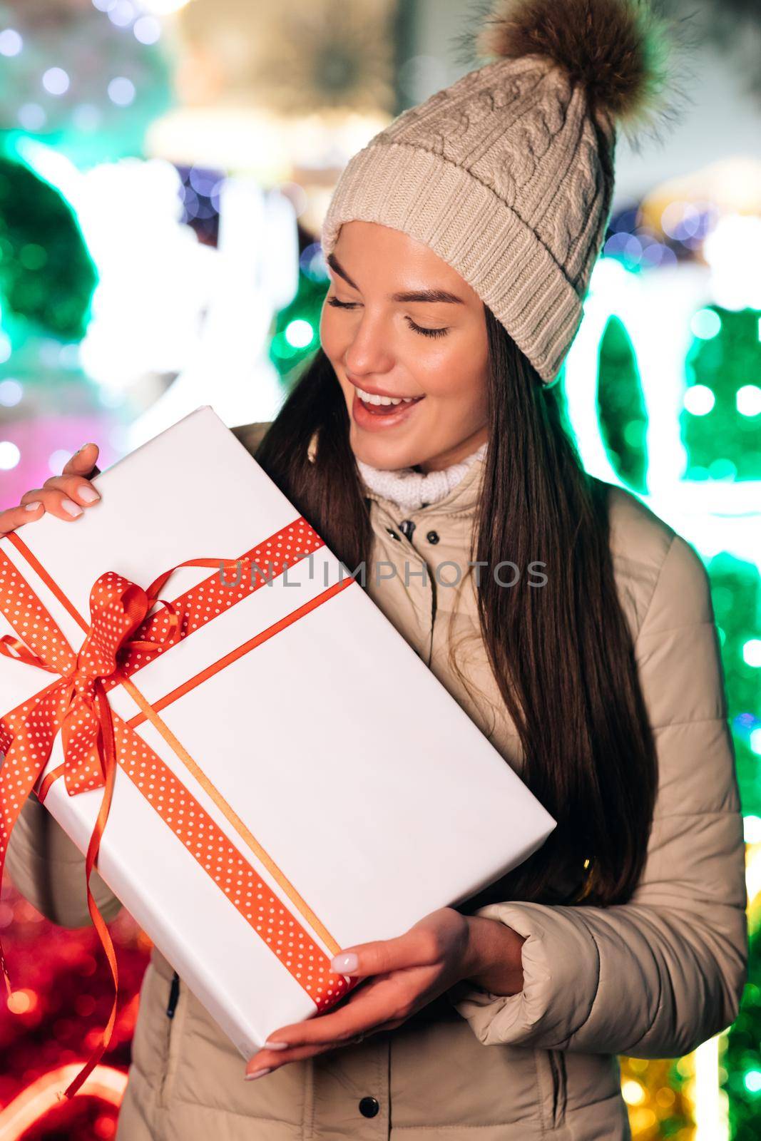 Portrait of happy young woman christmas present boxes. Happy young woman in hat holding christmas present box while standing on street. Winter concept.
