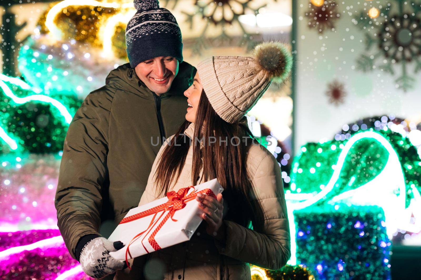 Close up of Young Beautiful Woman Hugging Man Holding Christmas Present. Pretty Girl Hugging With Boyfriend at Christmas Celebrating Holidays Together. Lovely Couple Stand. Gift Box Hugging Outdoors. by uflypro