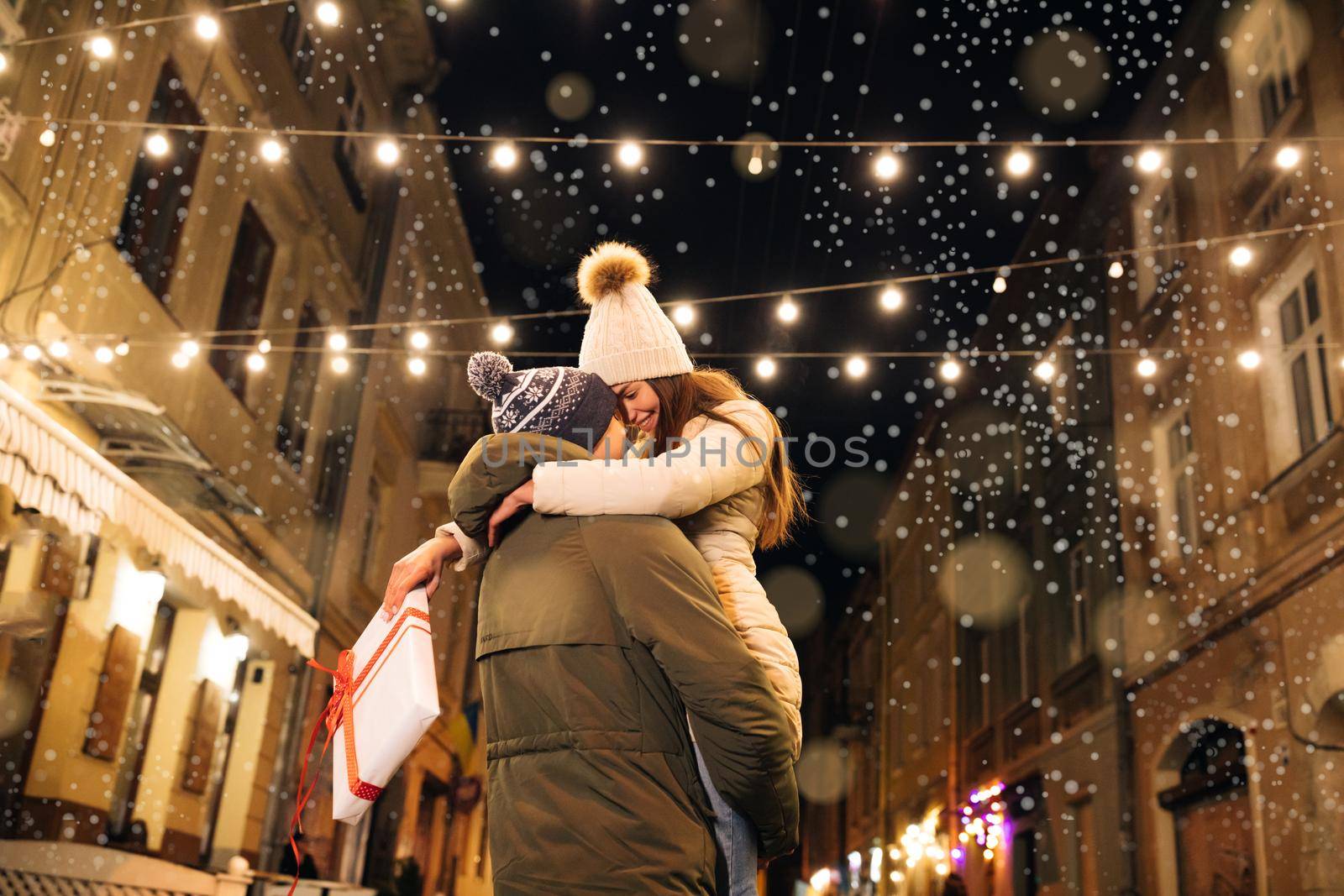 Beautiful love couple. Illumination. Happy Couple Outdoors. Attractive young woman meeting up with boyfriend on christmas evening party hugging tightly together swinging on the street.