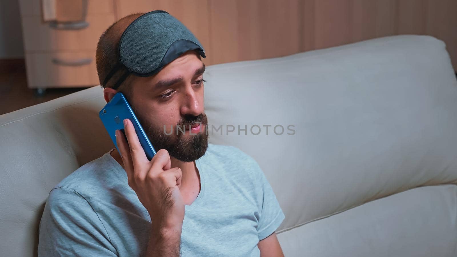 Close up of bored man talking on phone with collegue about social media, holding popcorn bowl in hands. Caucasian male sitting on couch in front of television late at night