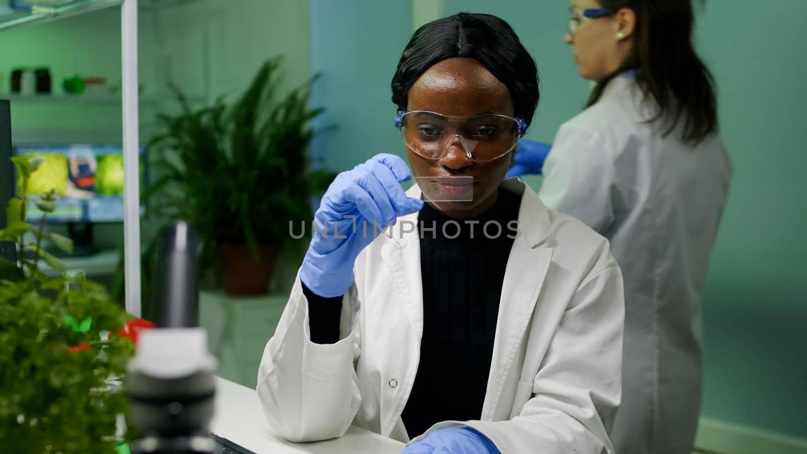 Botanist researcher scientist analyzing green liquid sample under microscope for microbiology experiment. Chemist specialist discovering organic gmo plants while working in pharmaceutical laboratory