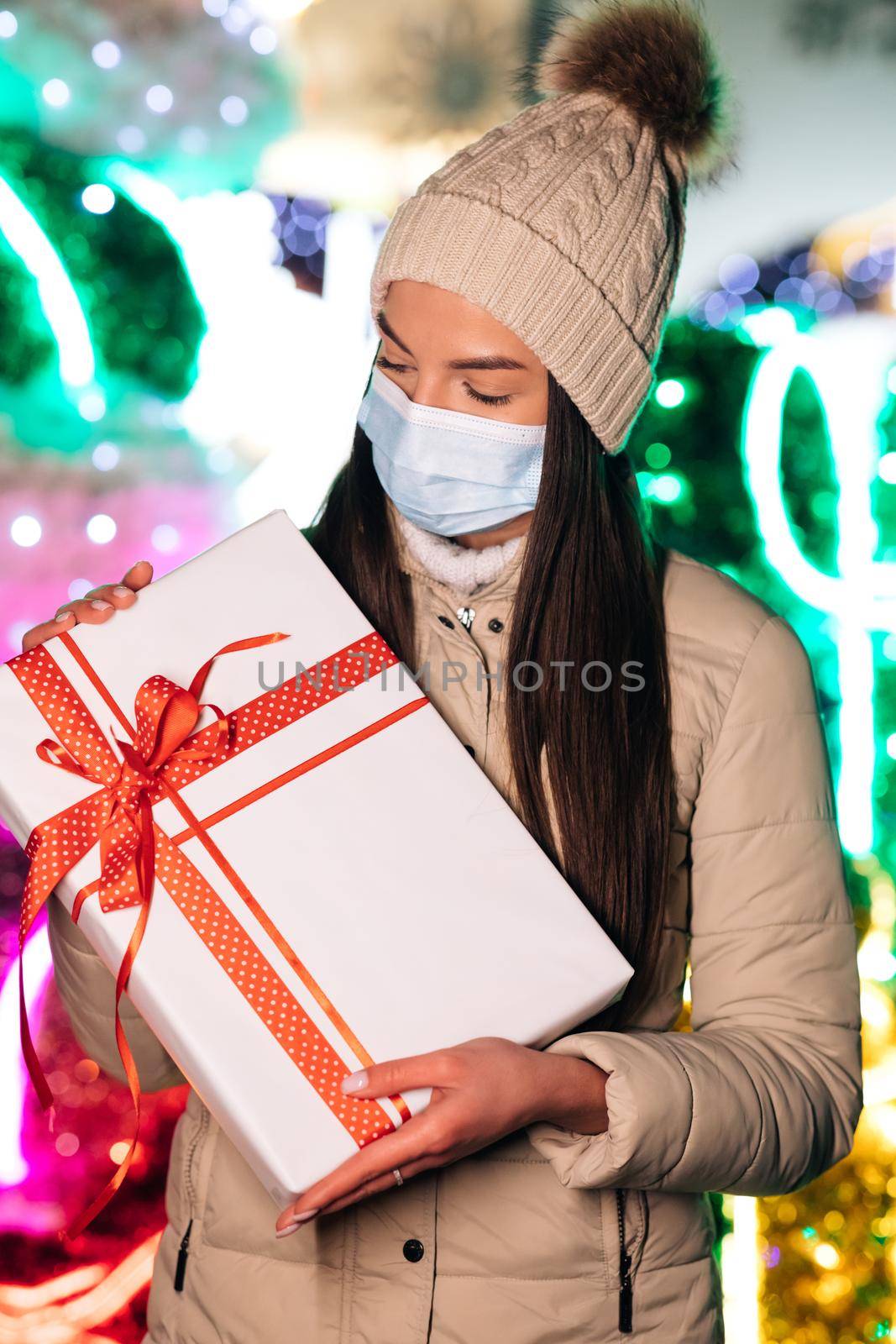 Portrait beautiful female in mask standing on street. Young woman with christmas present. Winter concept.
