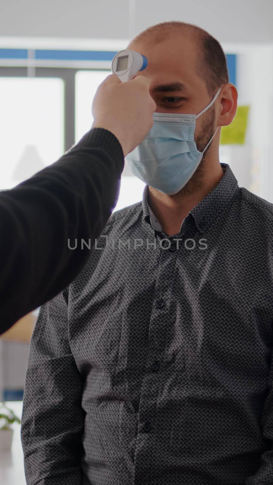 Freelancer man wearing protective mask against covid19 while checking temperature using medical thermometer to avoid infection with coronavirus. Company taking precautions during global pandemic