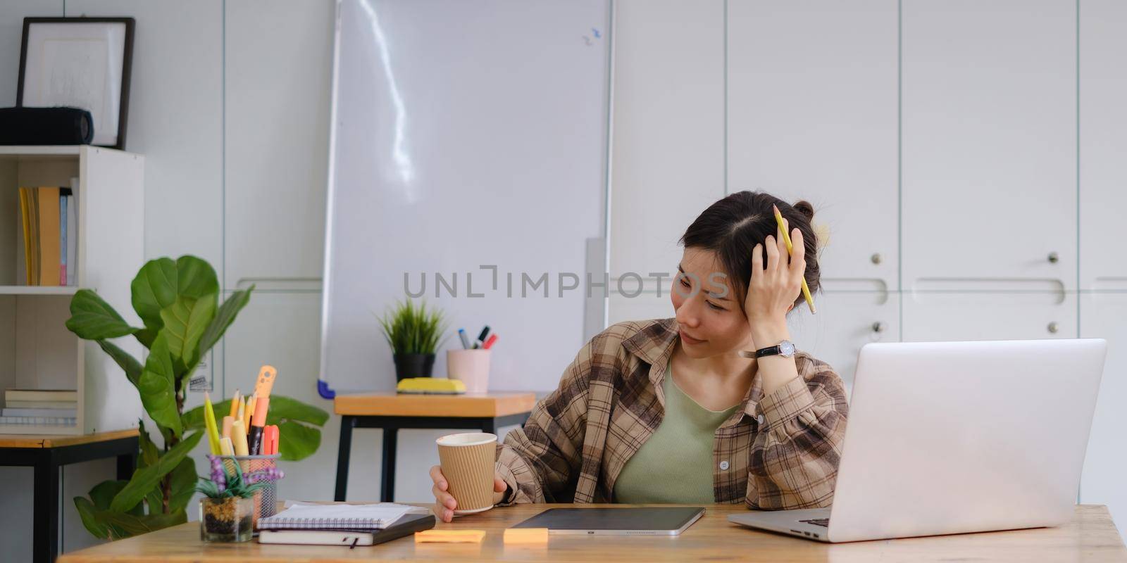 Portrait of cheerful asian woman with casual life with morning coffee and sitting on chair in home office. Concept of young business people working at home. by itchaznong