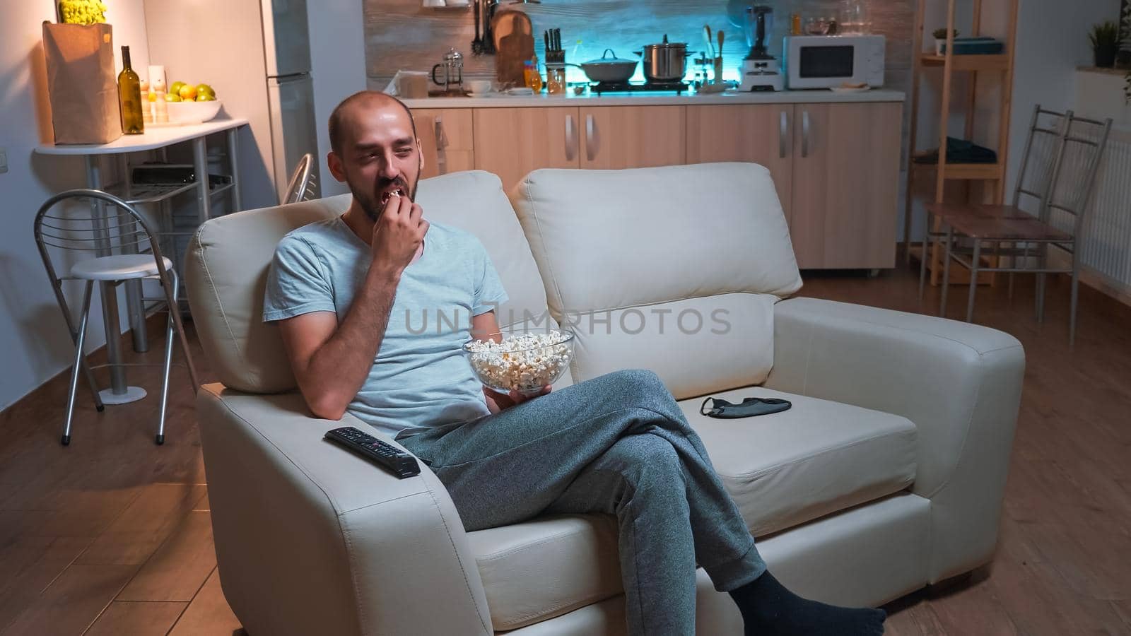 Man with beard watching tv show using remote control to change channels on television by DCStudio