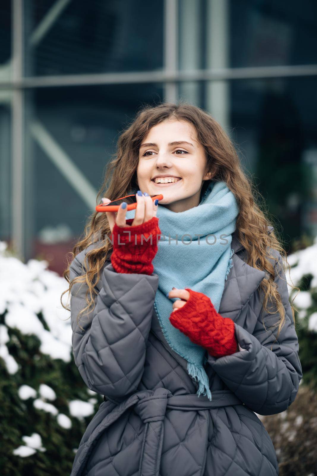 Portrait of Curly-haired Woman with phone using the voice recognition ai audio message on the phone, audio message ai speech helper. Vacation winter outdoor by uflypro