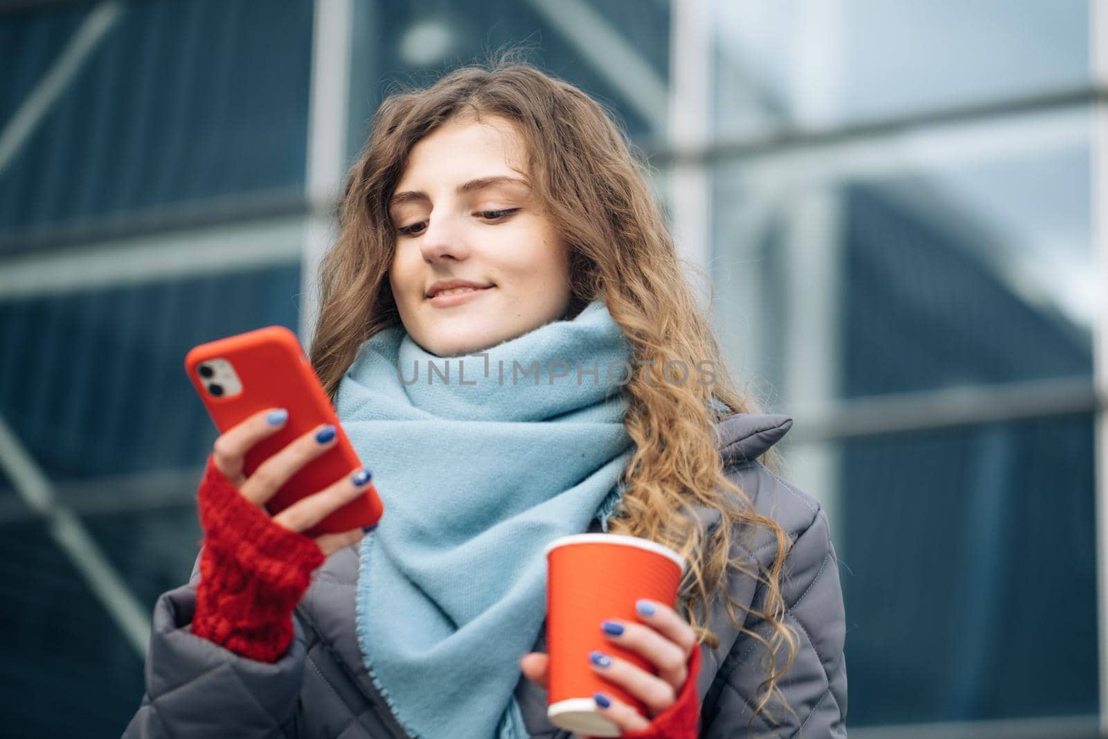 Portrait of happy beautiful curly woman with coffee cup takeaway use mobile phone texting messages. Woman look on the winter street city by uflypro
