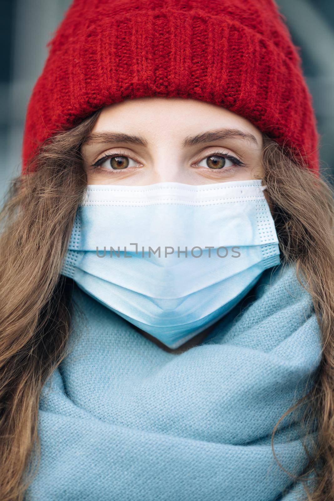 Close up portrait of Caucasian young curly female in medical mask standing in winter city. Crowd people sick covid-19. Epidemic coronavirus. Pandemic flu corona virus by uflypro