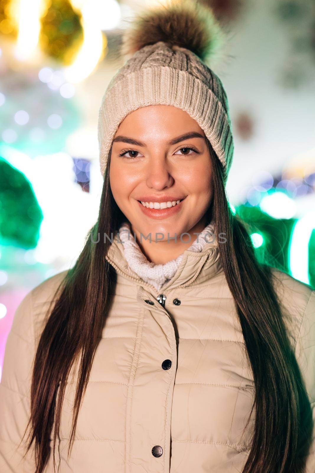 Portrait of joyful caucasian woman in hat looking at camera smiling around Christmas lights in city center. Positive mood happy emotion standing outdoor. Winter beautiful street face outdoor.