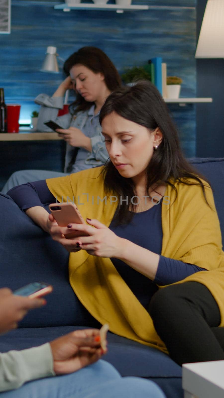 Multiracial friends relaxing on couch while surfing news on internet using mobile speding time together during surprise party. Group of multi-ethnic people watching online funny movie in living room