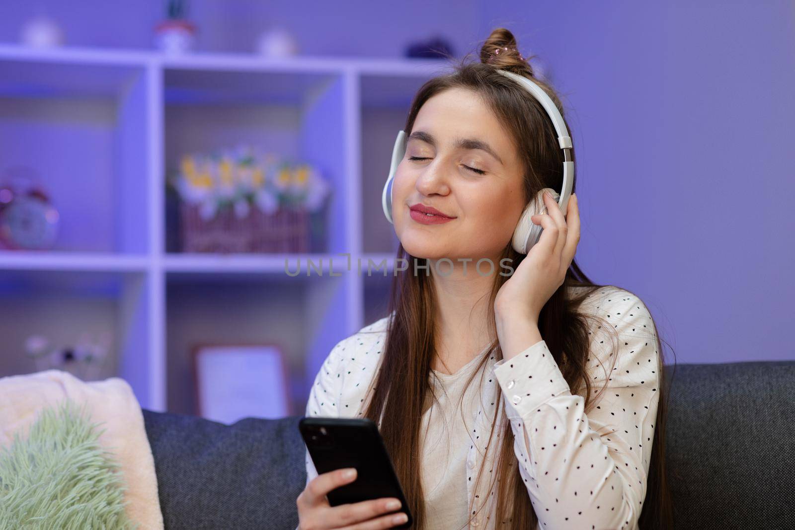 Attractive girl enjoying music through headphones sitting on sofa. Young Woman Listening To Music. by uflypro