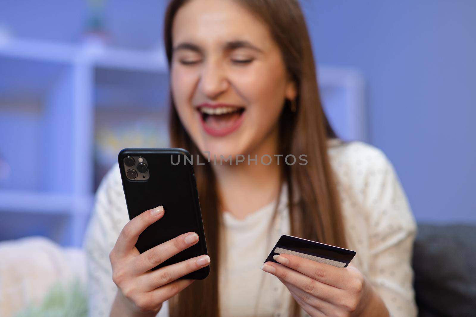 Online shopping concept. Young woman holding a credit card and doing online payment with smartphone at home