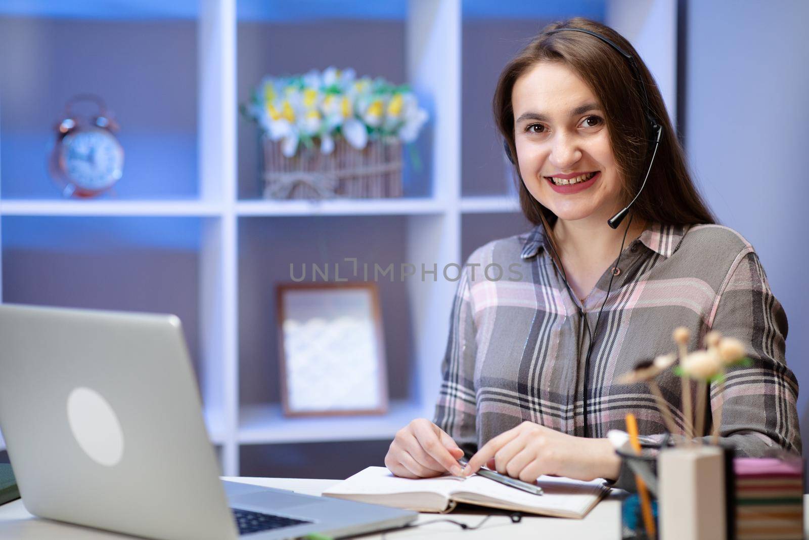 Smiling young woman student wear headset using laptop for e learning course online teaching in internet at home. Positive charming woman working at home.