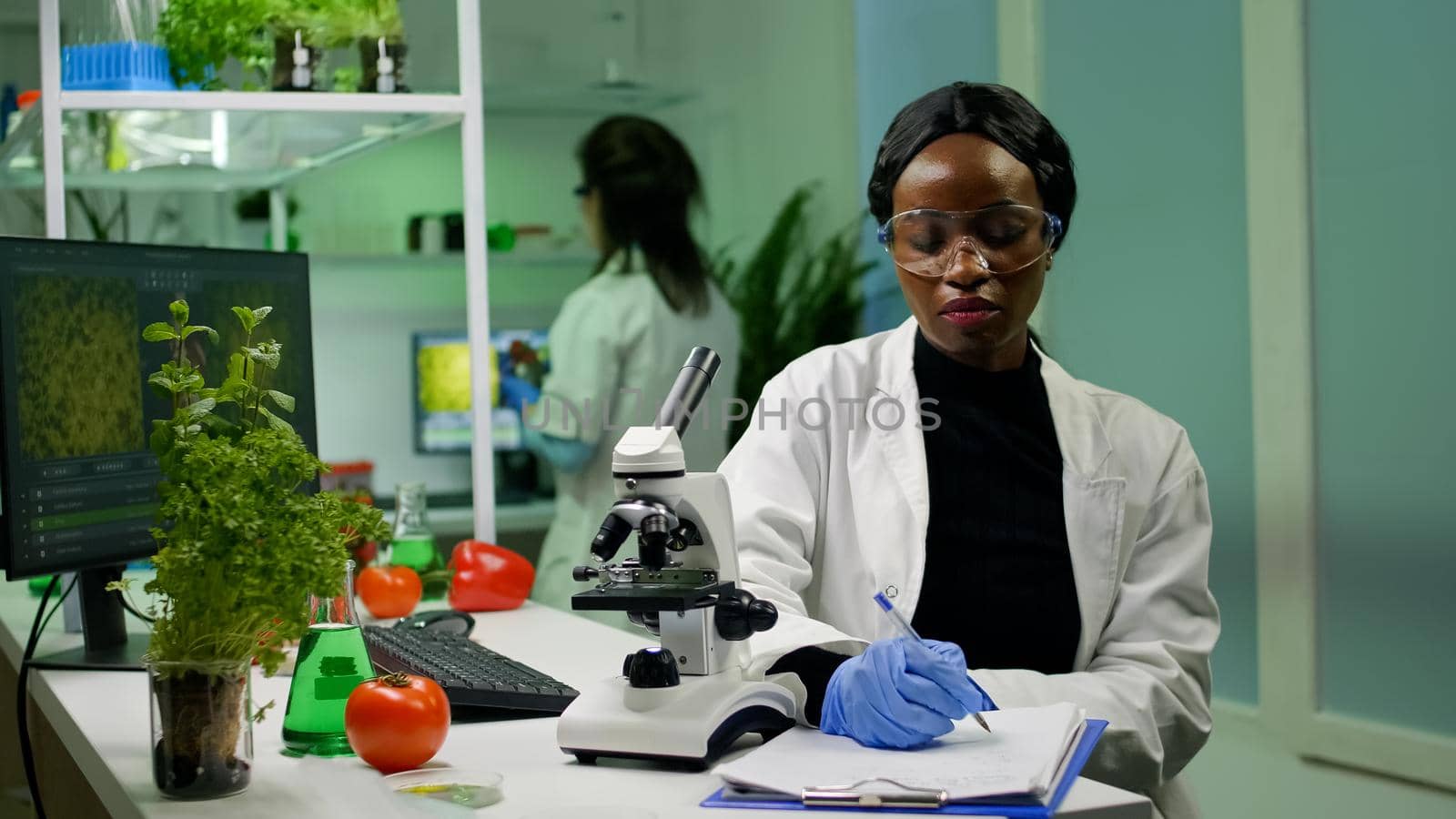 Biologist researcher scientist looking at leaf sample under medical microscope while writing biological expertise on notepad. Chemist examining biological discovery working in microbiology lab