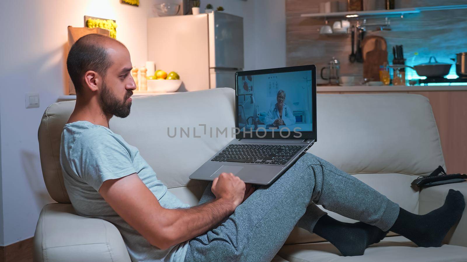 Physician doctor consulting sick patient during videocall consultation using laptop computer while standing on sofa. Caucasian man talking about illness symptoms and headlcare treatment