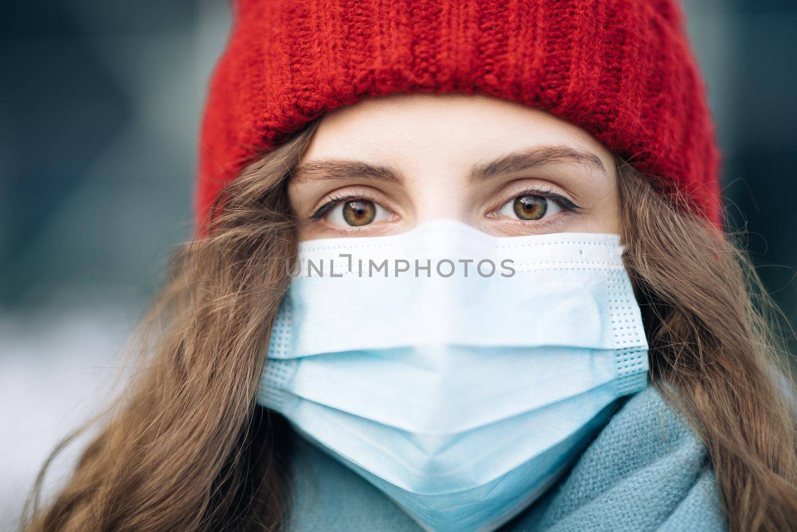 Portrait of Caucasian young curly female in medical face mask standing on winter street. Crowd people sick covid-19. Epidemic coronavirus. Pandemic flu corona virus.